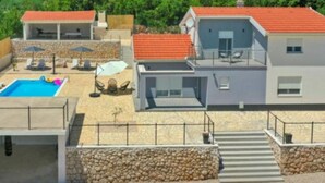 Et moderne hus med to etager, swimmingpool, udendørs møbler og en stenvæg.