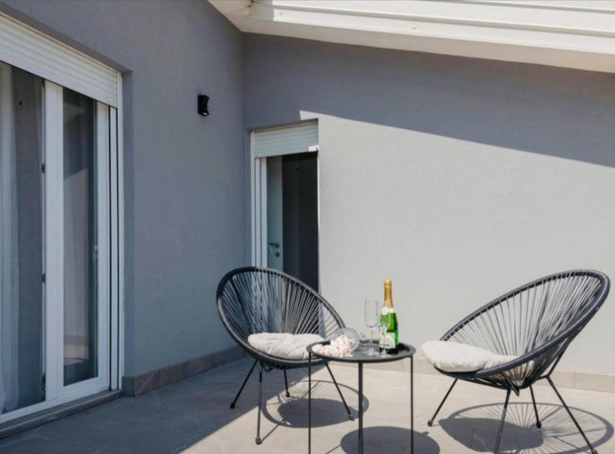 Un balcon avec deux fauteuils en osier, une petite table et une bouteille de champagne.