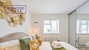Ein modernes Hotelzimmer mit Bett, Kissen, einer grünen Tagesdecke und einem Fenster mit Jalousien.