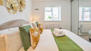A modern hotel room with a bed, pillows, a green throw, and a window with blinds.