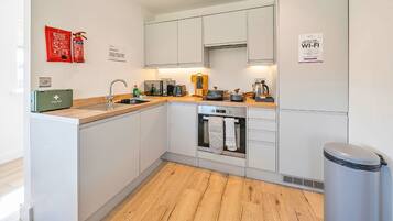 A modern kitchen with white cabinets, a built-in oven, and a stainless steel sink. There is a fire extinguisher and a first aid kit on the counter.