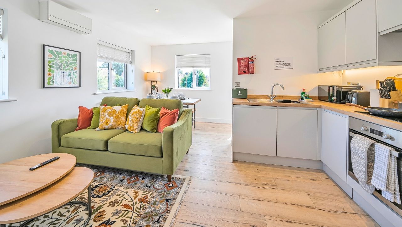 A modern kitchen with a built-in oven and a dining area with a green sofa and a wooden table.