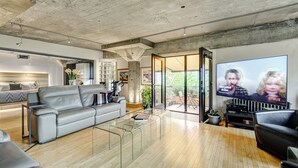 Un salon moderne avec un canapé gris, une table basse en verre et un téléviseur à écran plat diffusant une série Netflix.