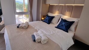 A hotel room with a large bed, two pillows, a nightstand, and a window with curtains. - Blue Charm Mobile Home (Orebic)
