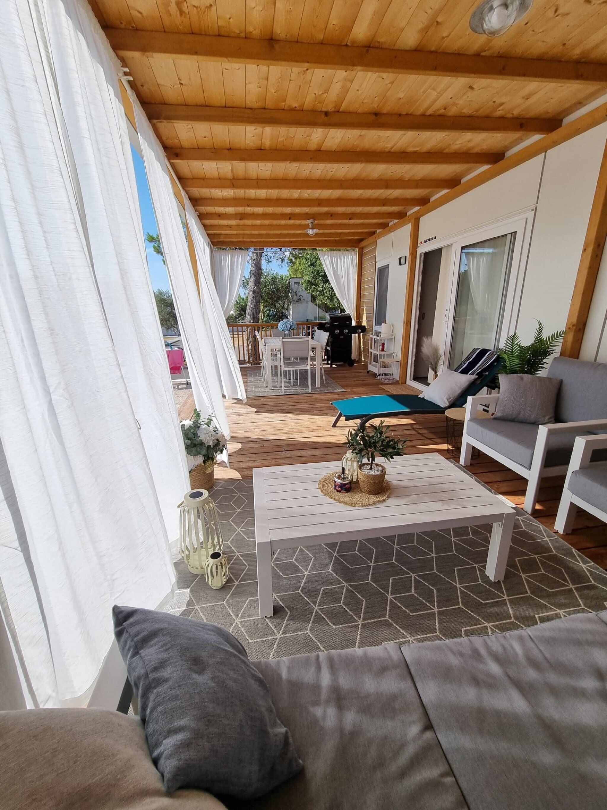 Un espace extérieur abrité, doté d’un plafond en bois, d’une table blanche et d’un canapé avec des coussins.