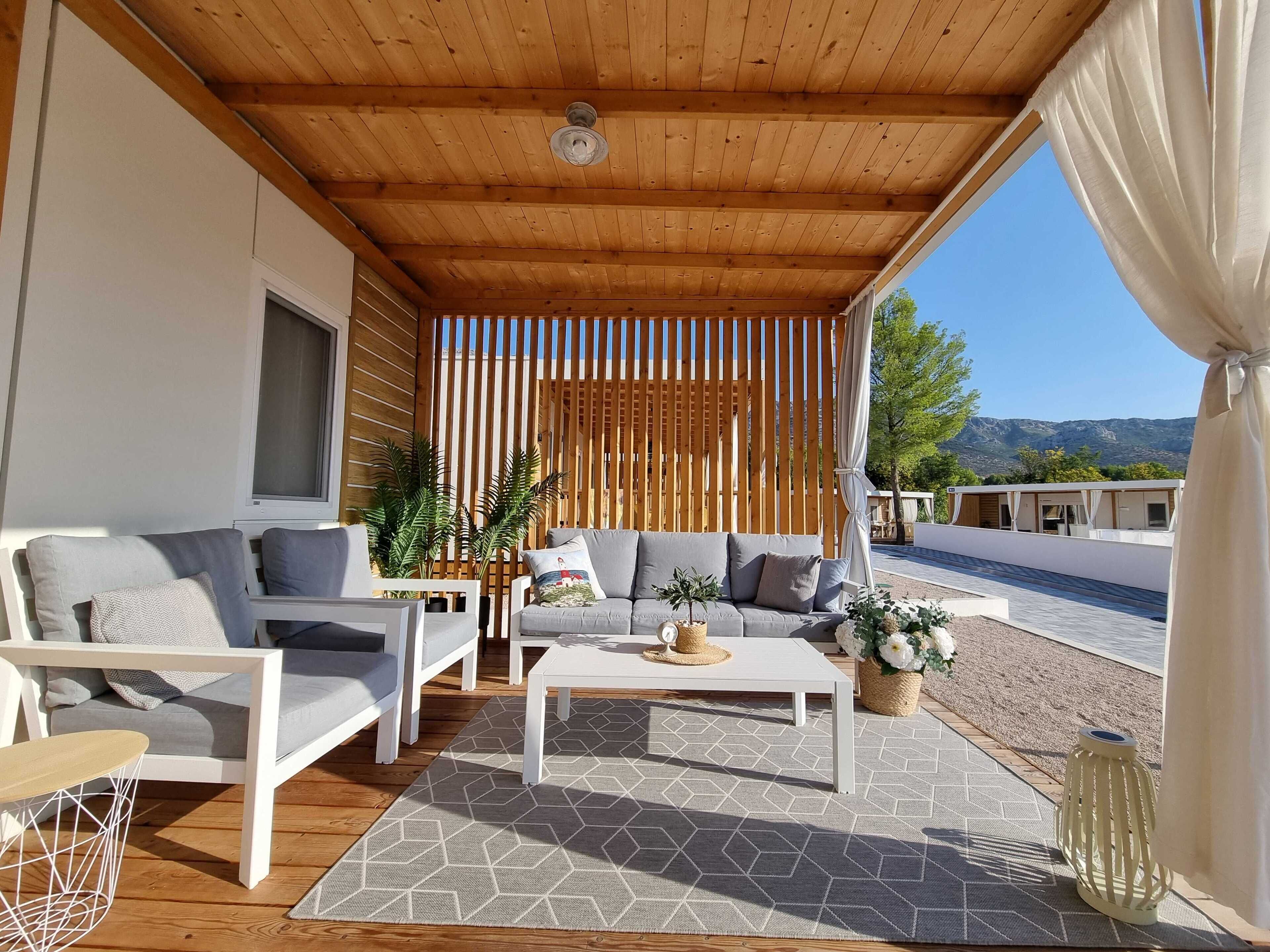 Un espace extérieur aménagé, abrité, avec un plafond en bois, un ensemble de canapés, une table basse et une vue sur la plage et les montagnes.