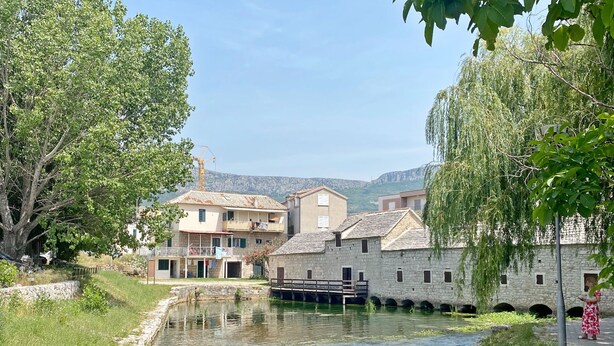 Un canal bordé de bâtiments en pierre, un pont et une personne vêtue d’une robe rouge.