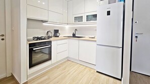 Une cuisine moderne avec des meubles blancs, un four encastré, une cuisinière à gaz, une machine à café et un réfrigérateur blanc.