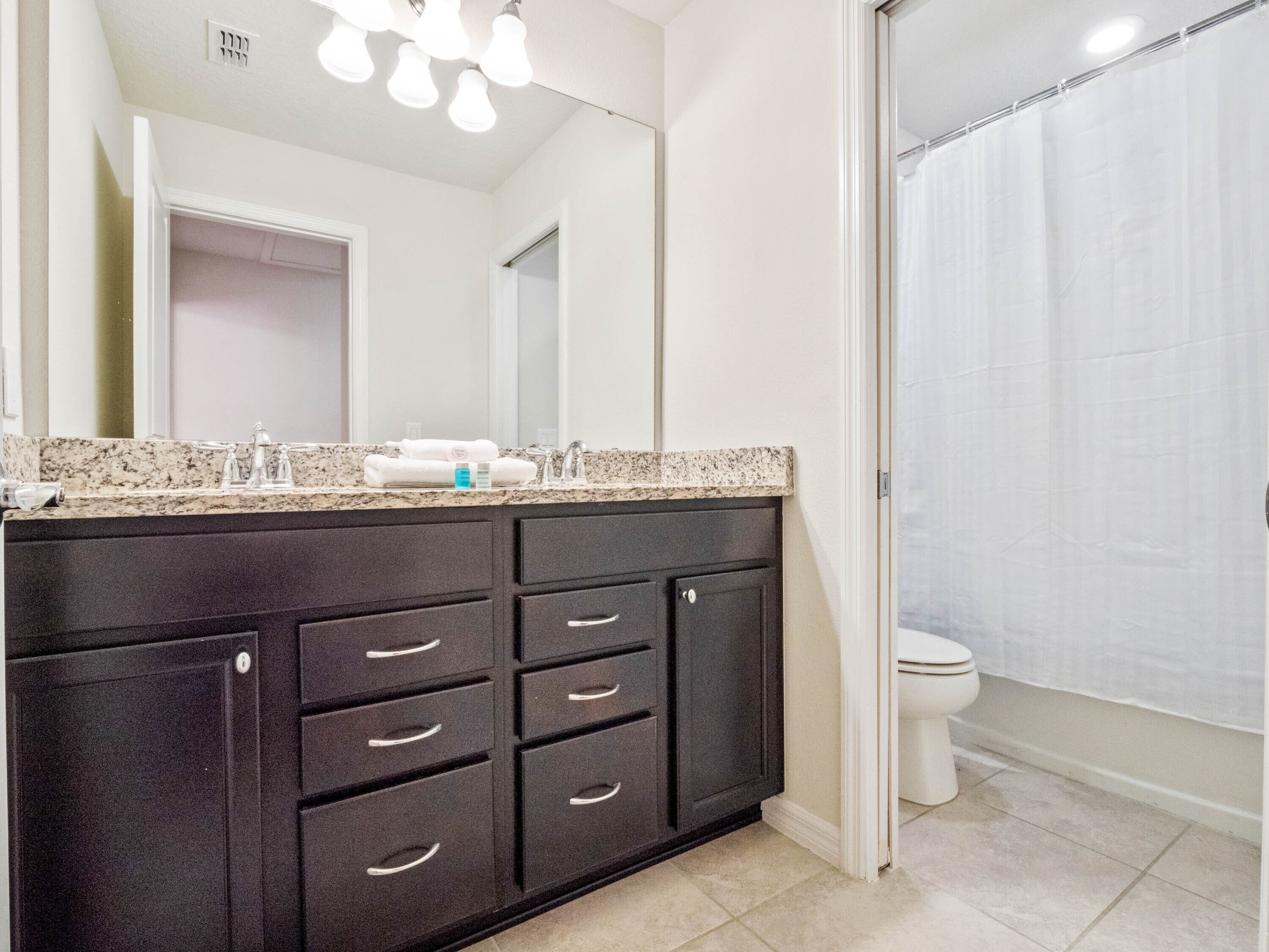 A modern bathroom with a dark wood vanity, a large mirror, and a shower curtain.