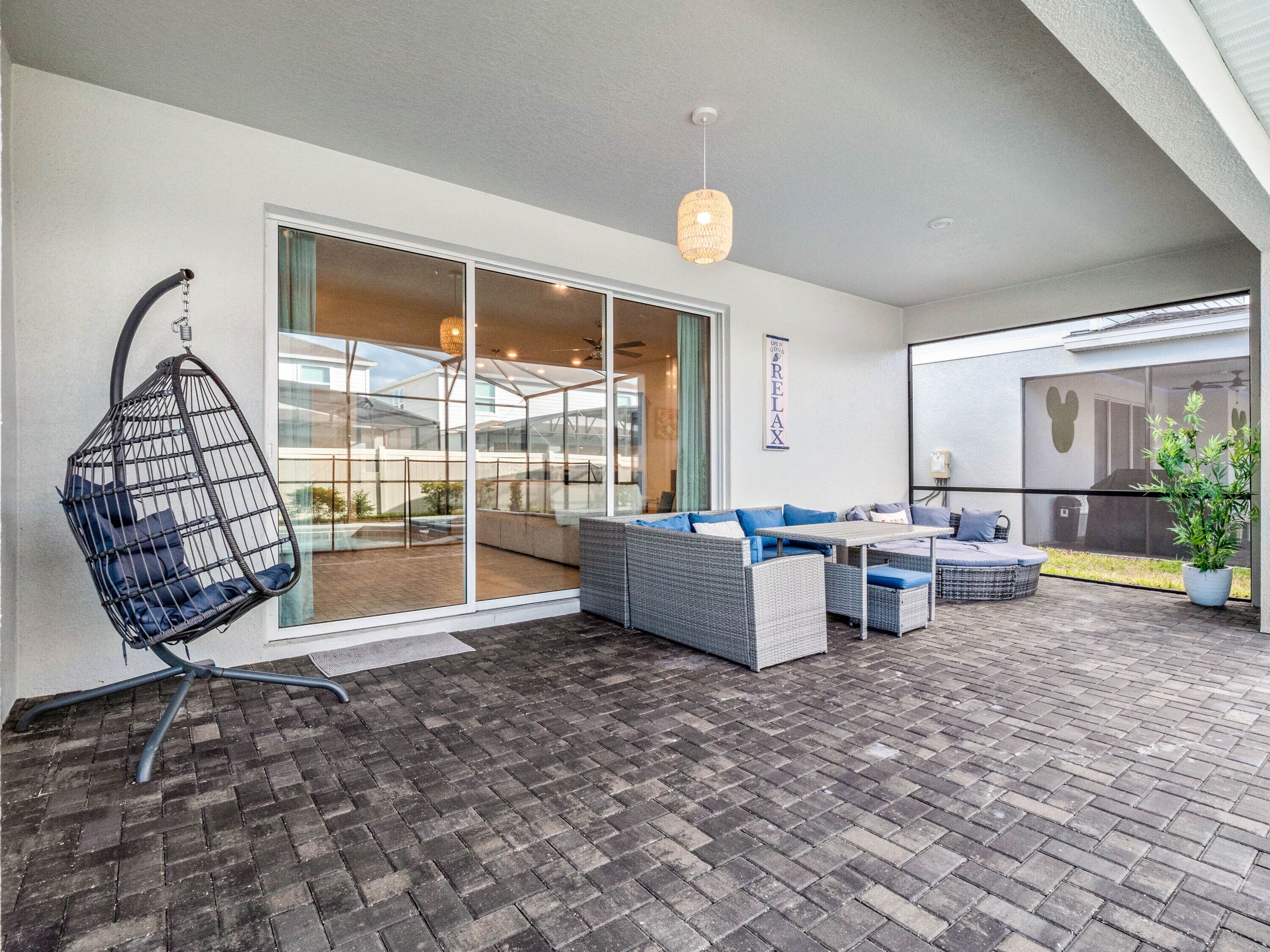 A modern outdoor patio with a hanging chair, wicker furniture, and a large sliding glass door leading to a covered area.