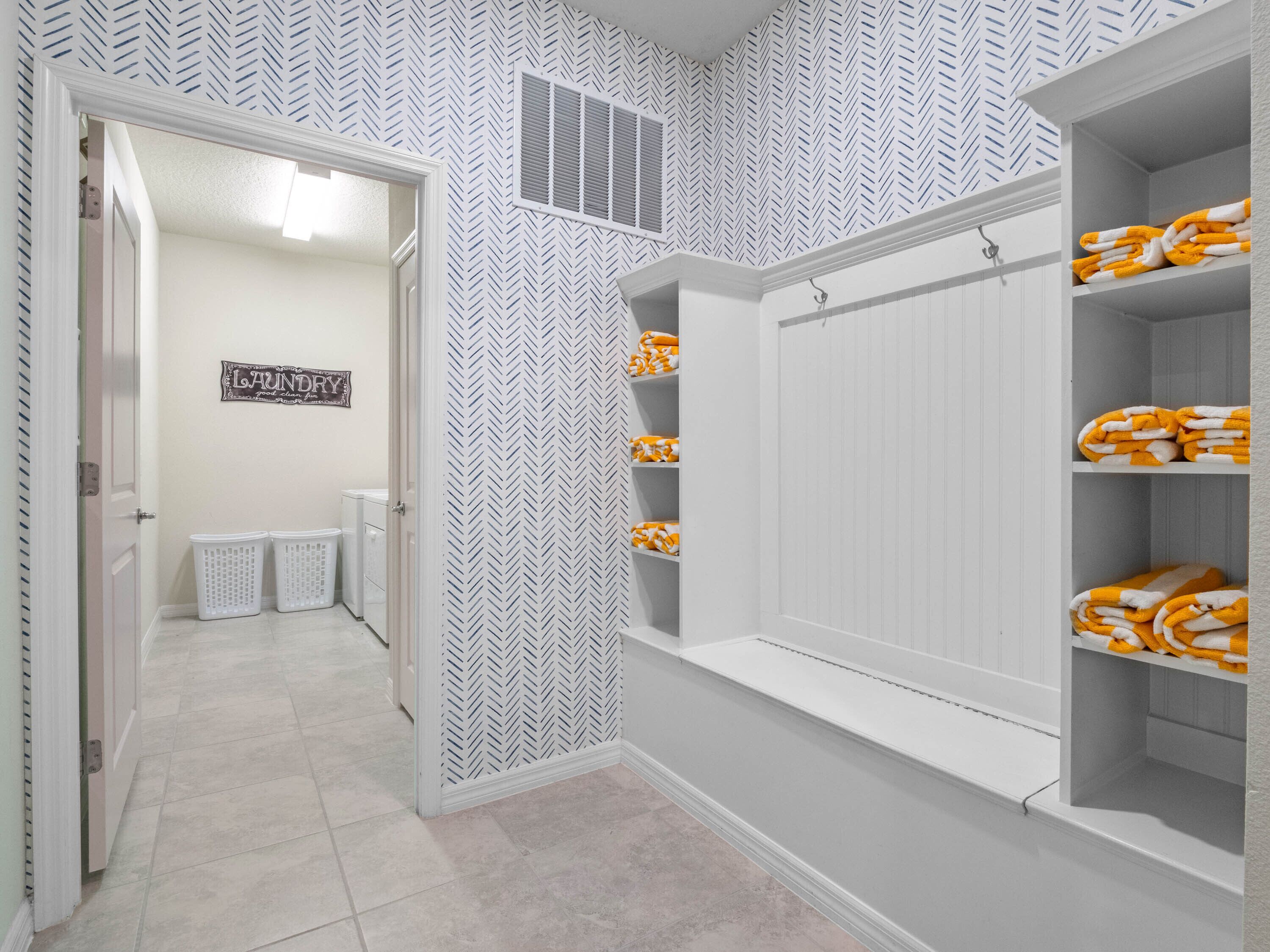 Een wasruimte met een muur in herringbone patroon, een bord met de tekst 'Laundry' en planken met opgevouwen handdoeken.