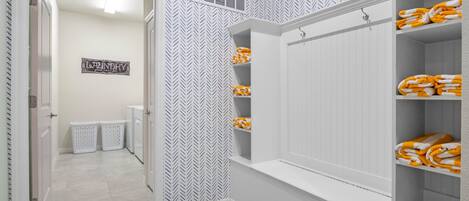 A laundry room with a herringbone patterned wall, a sign that says "Laundry," and shelves with folded towels.