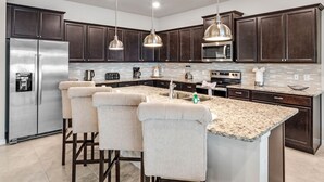 A modern kitchen with dark wood cabinets, stainless steel appliances, and a central island with bar stools. - Last Minute Disney! Private Pool, Hot Tub & Themed Bedrooms. Book Now! #108121 (Orlando)