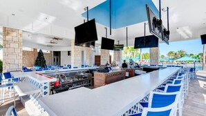 A modern outdoor bar area with a stone wall backdrop, multiple seating arrangements, and a Christmas tree. - Last Minute Disney! Private Pool, Hot Tub & Themed Bedrooms. Book Now! #108121 (Orlando)