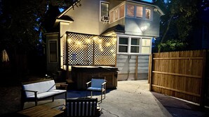 Un jardin avec un espace patio, des sièges d’extérieur et une clôture en bois.