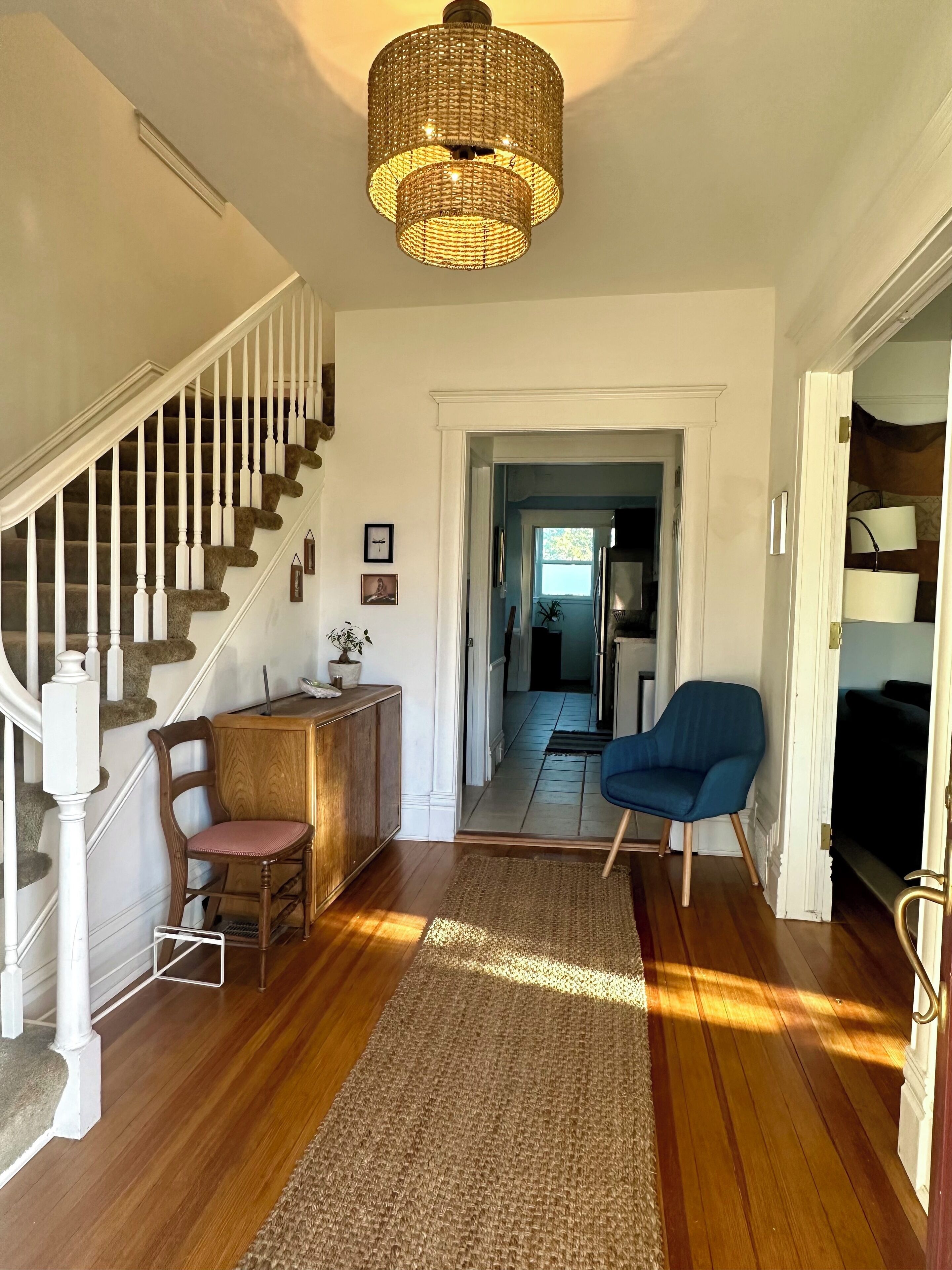 A staircase with white balusters, a wooden chair, a blue armchair, and a woven rug.
