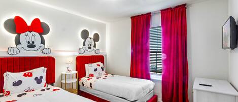 A hotel room with two beds, red curtains, and Mickey Mouse wall decorations.