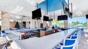 Un espace bar extérieur moderne, agrémenté d’un mur en pierre servant de décor, de plusieurs coins salon et d’un sapin de Noël.