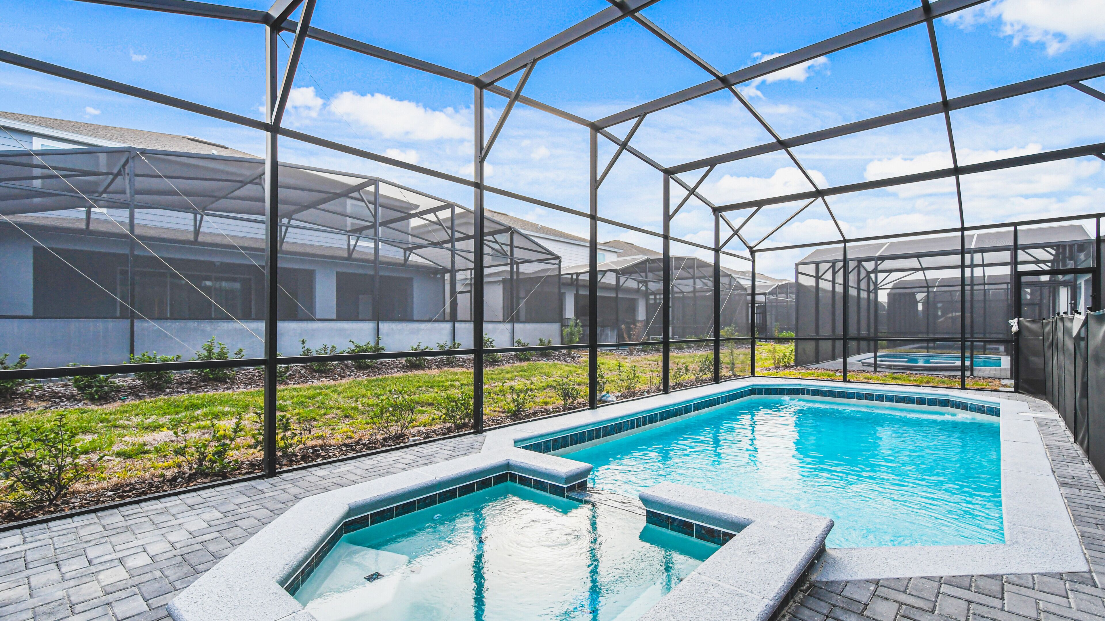 A swimming pool with a glass enclosure, surrounded by a brick patio and a greenhouse structure.