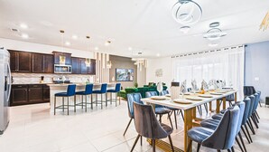 A modern kitchen with dark wood cabinets, a central island, and a dining area with blue chairs and a long table set for six.