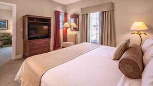 Habitación de hotel con una cama grande, televisor, escritorio y ventana con cortinas.
