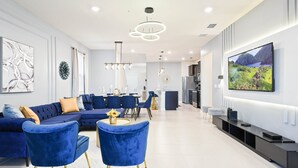 A modern living room with a sectional sofa, blue chairs, a dining area, and a kitchen in the background.