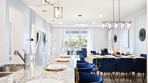 A modern dining area with a marble countertop, blue velvet chairs, and a large window offering a view of the outdoors.