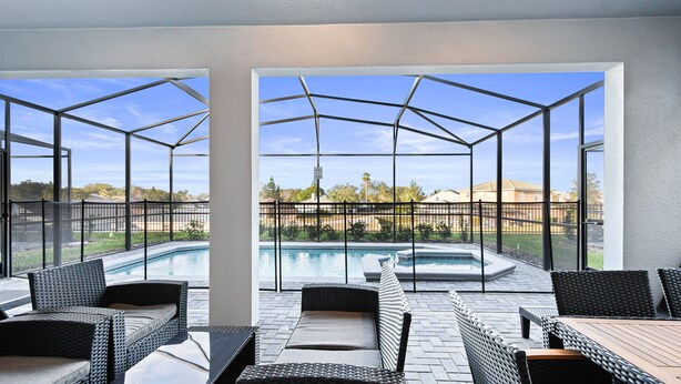 A covered outdoor area with a pool, wicker furniture, and a view of a residential neighborhood.