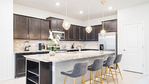 A modern kitchen with dark wood cabinets, a granite countertop, stainless steel appliances, and a central island with bar stools. - Last Minute Disney! Private Pool, Hot Tub, Game Room & Themed Bedrooms. Book Now! #111505 (Orlando)