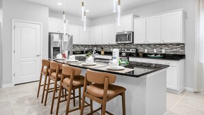 A modern kitchen with white cabinets, a black countertop, and a central island with bar stools. - Last Minute Disney Getaway! Villa with Private Pool & Hot Tub. Book Now! #114161 (Orlando)