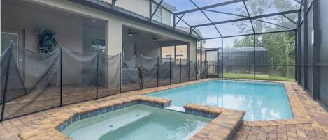 A covered swimming pool with a hot tub, surrounded by a fence and a brick patio.