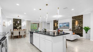 A modern kitchen with a central island, white cabinetry, and a dining area with a table and chairs. - Last Minute Disney Getaway! Villa with Private Pool & Hot Tub. Book Now! #114161 (Orlando)