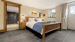 Een slaapkamer met een houten bed, een nachtkastje, een raam met gordijnen, een deur en een badkamer met douche.