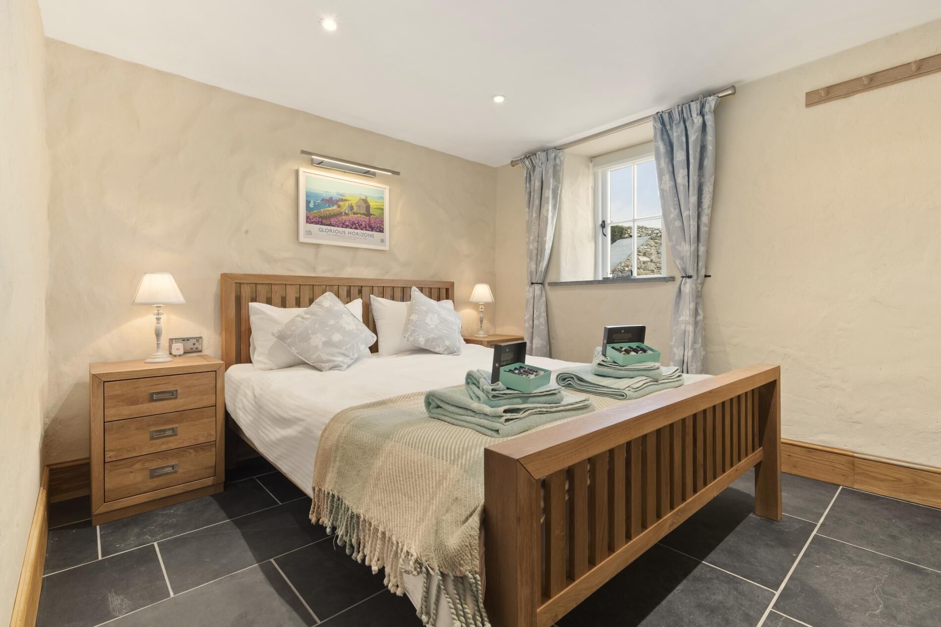 Une chambre à coucher avec un lit en bois, deux tables de chevet, une commode, une fenêtre avec des rideaux et un tableau au mur.