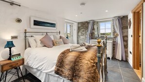 Un dormitorio con cama, mesita de noche, lámpara, manta de piel y ventana con cortinas.