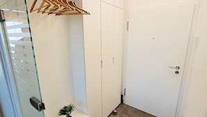 Ein heller, moderner Flur mit Glastür, Kleiderhaken und einem kleinen Topfpflanzen.