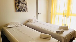 Ein Zimmer mit zwei Einzelbetten, einer Tür und einem Fenster mit gelben Vorhängen.