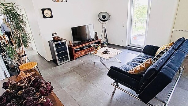 Ein modernes Wohnzimmer mit einer Couch, einem Fernseher und einem Essbereich mit Tisch und Stühlen.