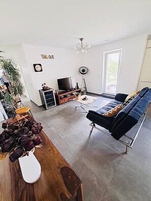 A modern living room with a sofa, TV, and a dining area with a table and chairs.