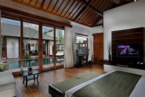 Ein Schlafzimmer mit Bett, Fernseher, Schreibtisch und Blick auf einen Pool.