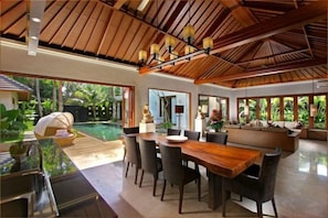 A spacious dining area with a wooden table and chairs, a large window, and a view of a swimming pool.