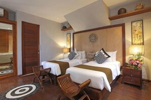 Ein Hotelzimmer mit zwei Betten, Holzboden, einem runden Teppich und einem Nachttisch mit Lampe und Blumen.