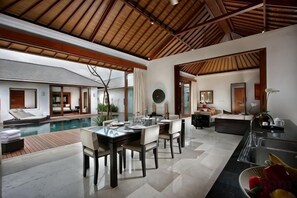 Espaço moderno de piscina interna com mesa e cadeiras, cozinha e área de estar com vista para a piscina.