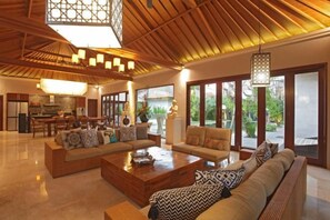 A spacious living area with a high ceiling, a dining area, and large windows offering a view of the outdoors.