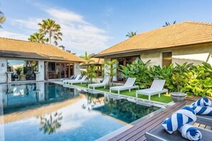 Un espace aménagé au bord de la piscine, avec des chaises longues, une piscine et un bâtiment doté d’un toit recouvert de tuiles.