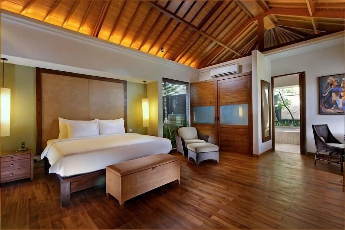 Een slaapkamer met een groot bed, houten plafond, een stoel en een bureau.