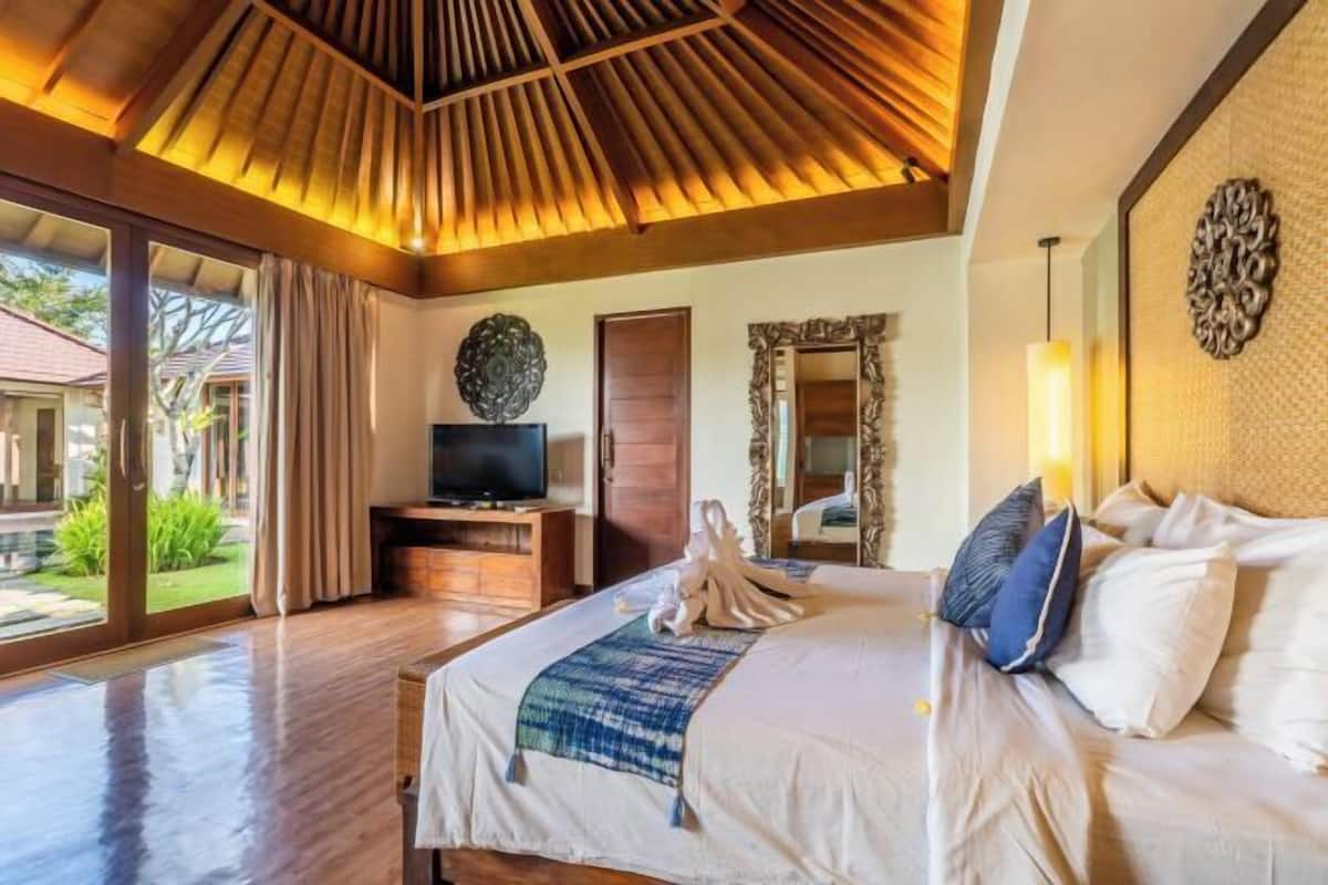 Een hotelkamer met een groot bed, een televisie op een houten dressoir, een spiegel en uitzicht op de omgeving.