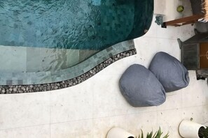 A swimming pool with a tiled edge, two grey bean bag chairs, and potted plants.