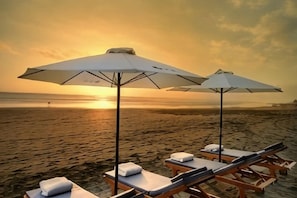 Ein Strand mit Liegestühlen und Sonnenschirmen, ein Sonnenuntergang im Hintergrund und ein ruhiges Meer.