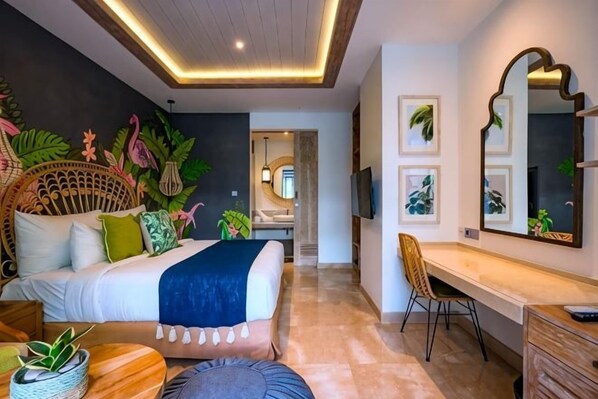 A modern hotel room with a bed, desk, and seating area, featuring a ceiling with recessed lighting and a large mirror.